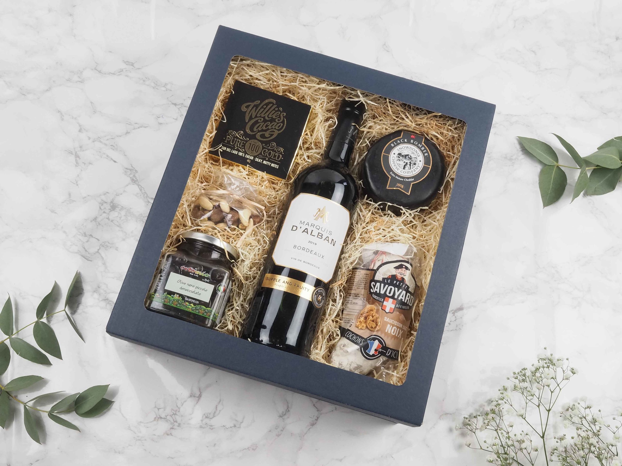 Dárková krabička v sobě ukrývá červené víno Bordeaux Marquis, 100% hořkou čokoládu Willies, mix oblíbených oříšků, černé olivy z Itálie, sýr cheddar Black Bomber a francouzský savojský salámek. Všechny pochutiny jsou baleny v elegantní a ekologické papírové krabičce. Obdarujte s chutí malým degustačním zážitkem.