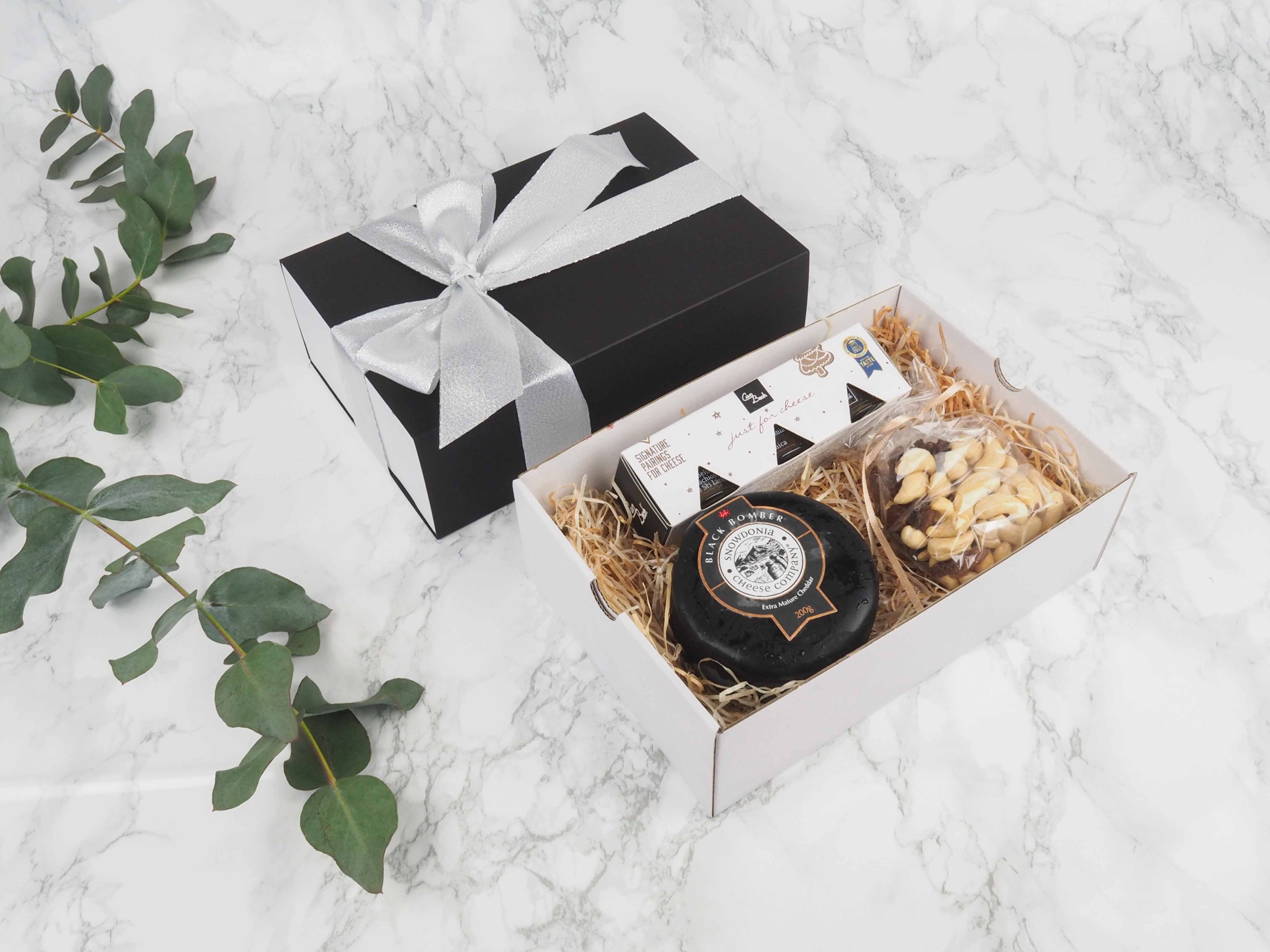 Dárkový balíček Black Exclusive je speciální svou elegantní vysouvací krabičkou, kterou zdobí atlasová stuha. Dárková krabice v sobě obsahuje britský sýr cheddar Black Bomber, mix oříšků a sadu ovocných mini omáček s příchutí perníčku.